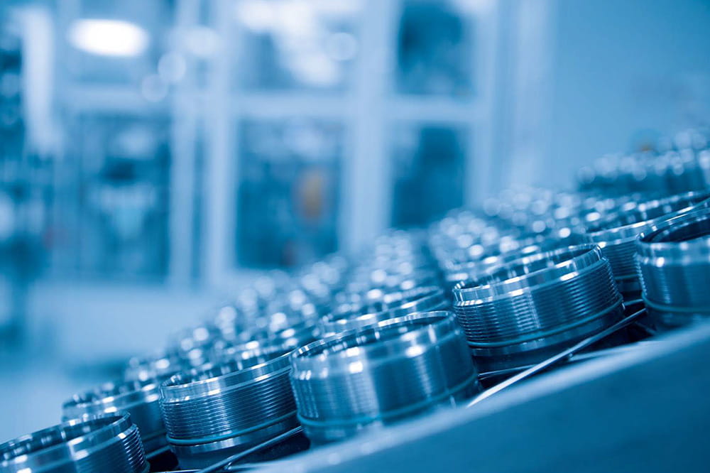 Close-up of metal components with threaded edges aligned on a conveyor belt in a factory, under a blue-tinted light, conveying precision and industrial efficiency.