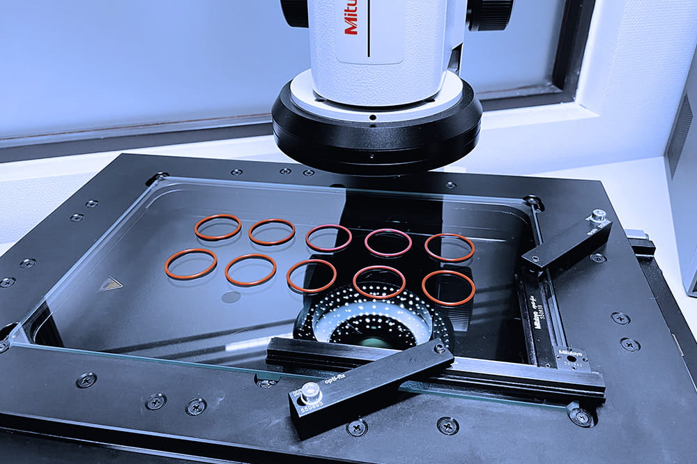 Microscope inspecting red rubber O-rings on a glass surface, under soft lighting. The setup suggests a meticulous and analytical environment.